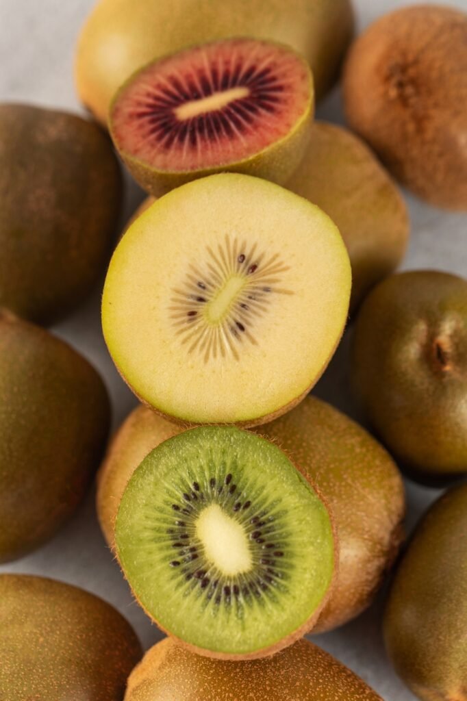 Different varieties of kiwi lie in a pile on the table. Halves of red, yellow and green kiwi.